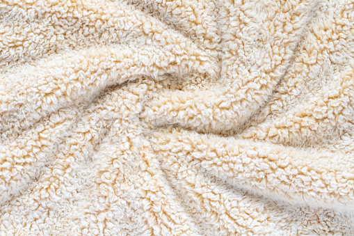 Beige soft plush fabric of comfy throw. Swirled warm blanket background.