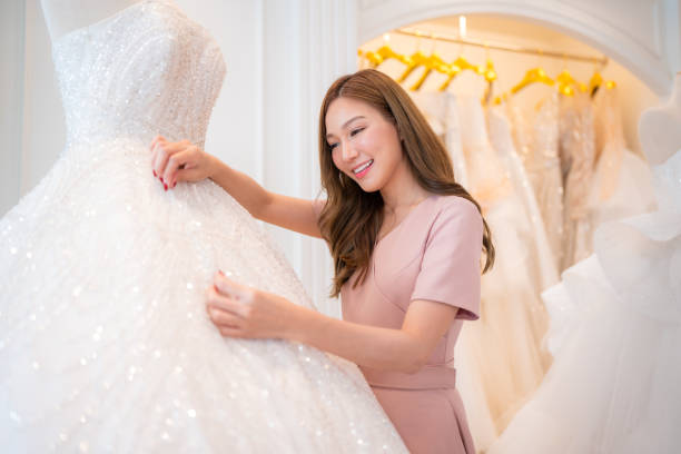 istock Attractive young bride is smiling while choosing wedding dress in modern wedding salon. 2151048817