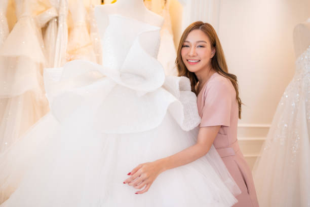 istock Attractive young bride is smiling while choosing wedding dress in modern wedding salon. 2151048833
