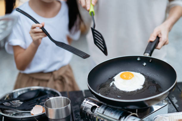 Asian mother and daughter making sunny side up egg with cooking pan