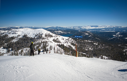 Soda Springs, CA, U.S.A. - April 1, 2024: Skiiers head down Mt. Lincoln to the Lake View intermediate run at Sugar Bowl Ski Resort. Donner Lake is in the background.