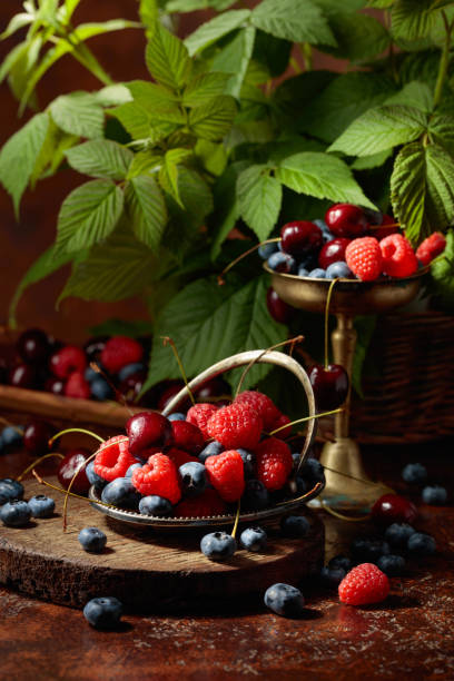 Berries with leaves on an old brown table. Colorful assorted mix of blueberries, raspberries, and sweet cherries.