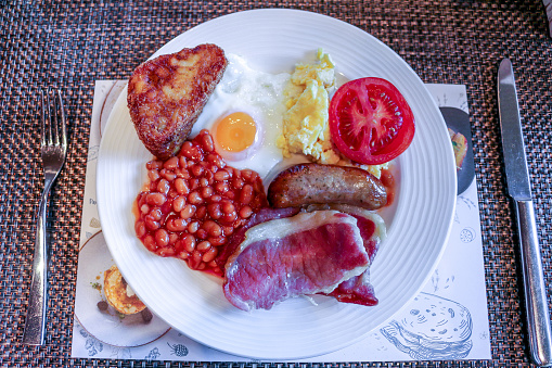A Full English Breakfast, bacon, sausage, beans, tomato, egg and hash brown with knife and fork