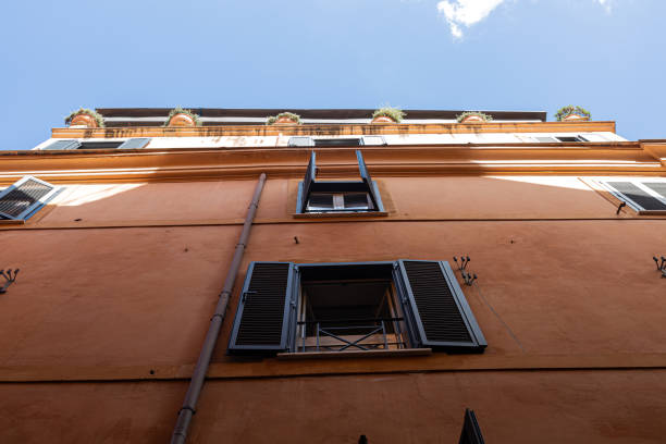 A picturesque courtyard in Rome, showcasing the warm tones of terracotta and cream on its walls. The open shutters and small balconies, adorned with plants, add a touch of charm to the historic architecture. A lamp post in the foreground anchors the scene, inviting visitors to look up and admire the beauty of everyday Roman life.