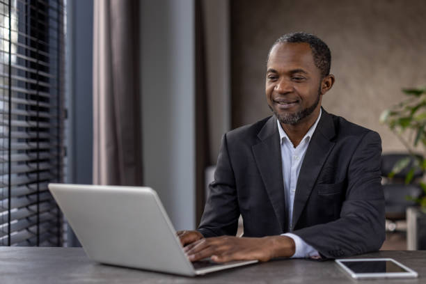 istock Grown up stylish man using portable gadgets for work in spacious apartment with window and plants. Progressive manager setting workspace at home and getting along with modern technology 2151062625