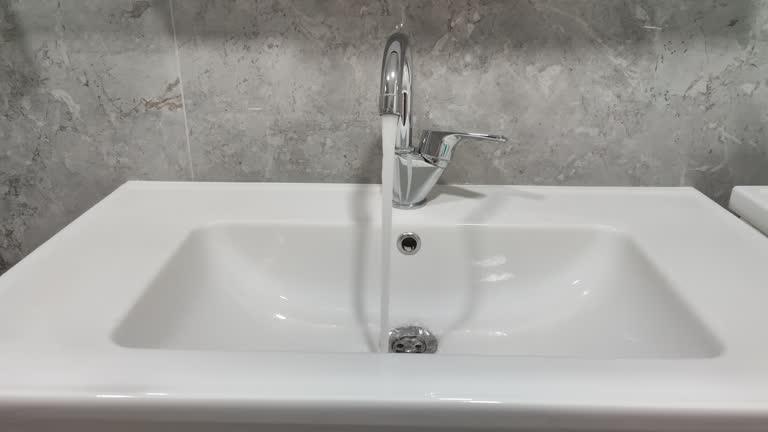 Water running continuously from water tap 4K. Open chrome faucet washbasin in bathroom.
