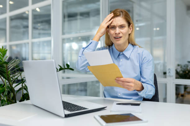 istock Shocked woman in formalwear touching forehead with arm while reading letter from open envelope in working space. Overworked manager receiving postal mail with warning from bank about debt payment 2151068712