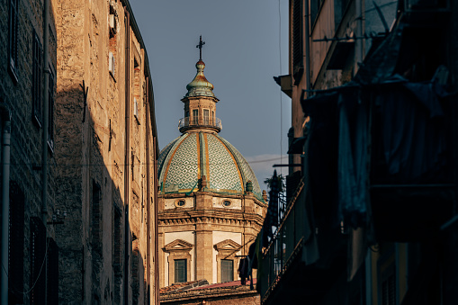 View of the cupola of Chiesa del Gesù in sunset seen between old buildings in Palermo, Sicily, Italy