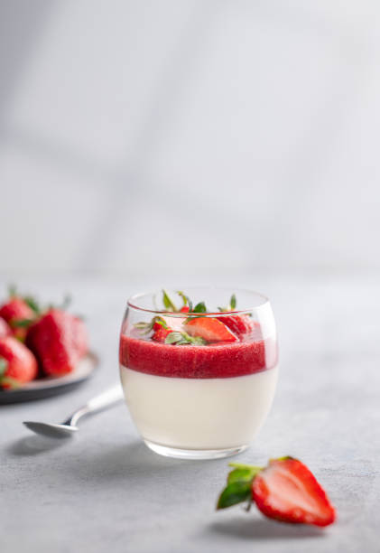 Panna cotta with strawberry and cream in glass with fresh berries on a light background close up with shadow.