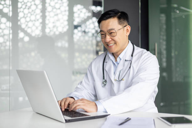istock Smiling Asian mature doctor working on laptop in office 2151074362