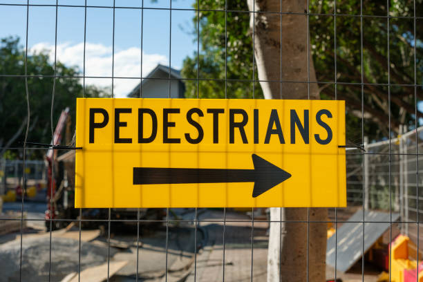 Yellow direction sign for pedestrians on a wire fence at a construction site.