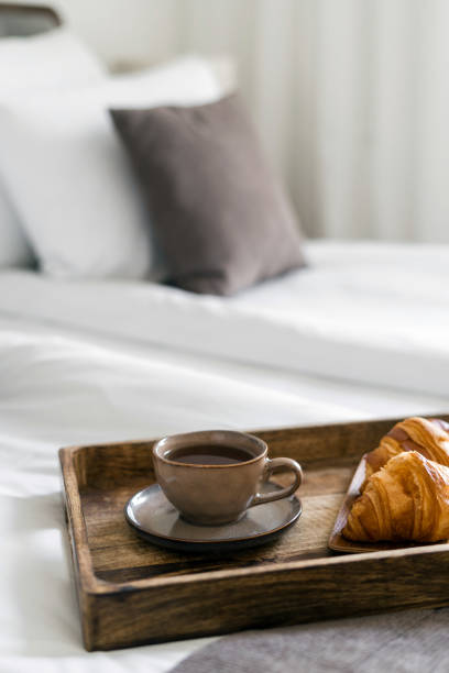 Wooden breakfast tray with coffee cup and croissants on bed