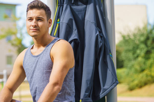 Handsome guy relaxing after outdoor workout. Fit man feeling healthy, enjoying sun. Exercising on public gym equipment in the open air.