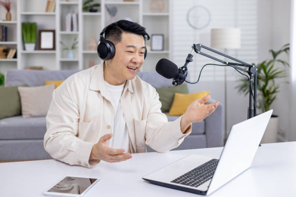 istock Smiling man podcasting from home with laptop and microphone 2151077555