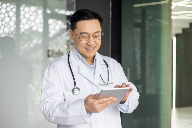 istock Smiling Asian doctor using tablet in modern hospital corridor 2151078250