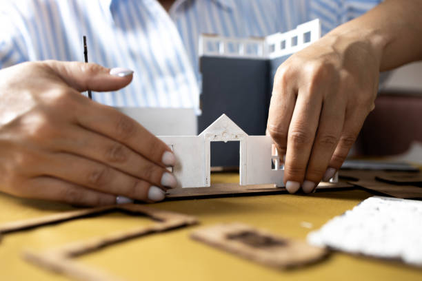 istock A girl assembles a model of a building from thick cardboard. 2151080283