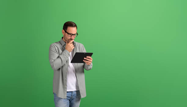 istock Thoughtful businessman with hand on chin analyzing strategy over digital tablet on green background 2151088127