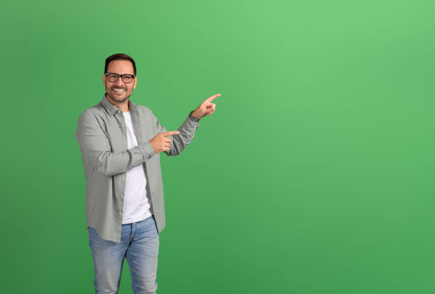 istock Handsome young man smiling and presenting copy space for advertisement on isolated green background 2151088201