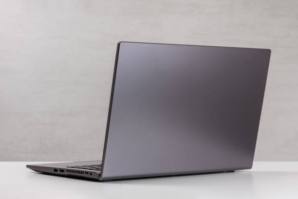 open silver laptop on a white table against a gray wall rear view with a copy space