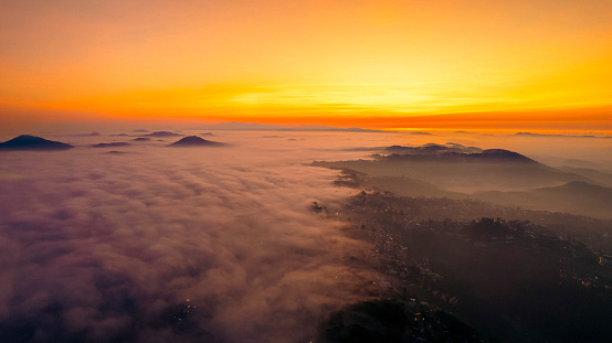 An aerial view of a city at sunset, with fog in the valleys and mountains in the distance.