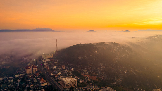 An aerial view of a city at sunset, with fog in the valleys and mountains in the distance.
