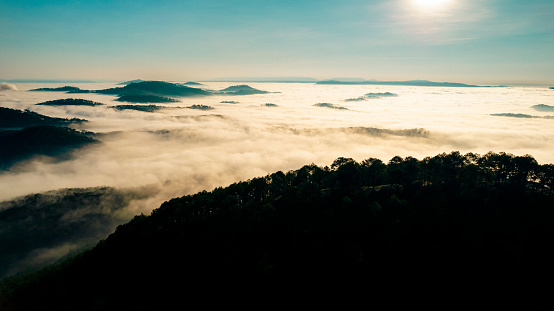 A sea of fog fills a valley, with lush green mountains rising in the background.