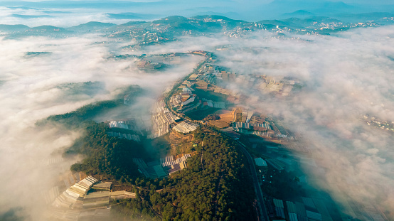 aerial view captures mist-covered mountains with patches of greenery and structured agricultural fields, showcasing nature’s beauty intertwined with human cultivation.