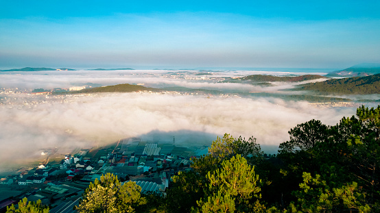 An aerial view of a city in the morning. The city is surrounded by clouds.