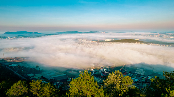 An aerial view of a city in the morning. The city is surrounded by clouds.