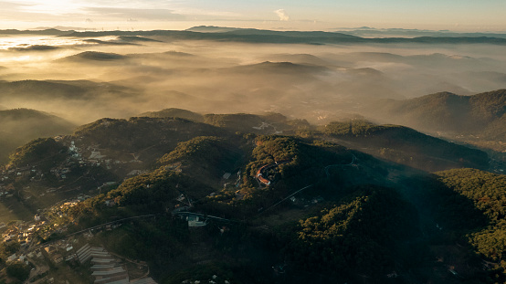 Aerial view of Dalat City at dawn, showcasing mist-covered mountains, lush greenery, scattered buildings, and serene atmosphere creating a picturesque landscape