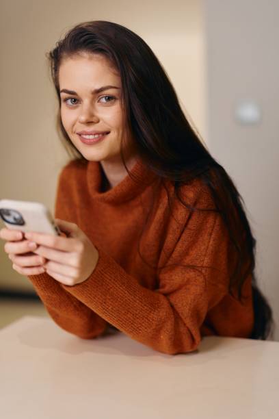 istock Beautiful Woman Sitting at Home, Holding and Using Mobile Phone, Happy and Relaxed While Chatting Online 2151102137