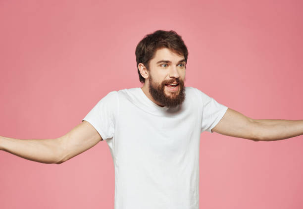 istock A man with a beard in a white T-shirt on a pink background gestures with his hands 2151108268