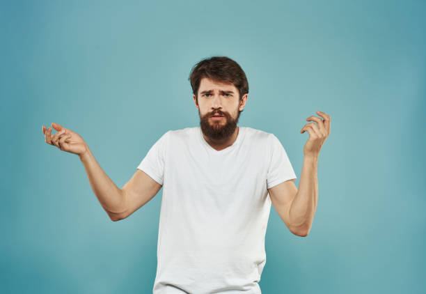 istock A man in a white T-shirt and with a thick beard on a blue background gestures with his hands 2151108789