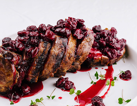 Juicy pork tenderloin topped with a rich cherry sauce, garnished with herbs on a white plate