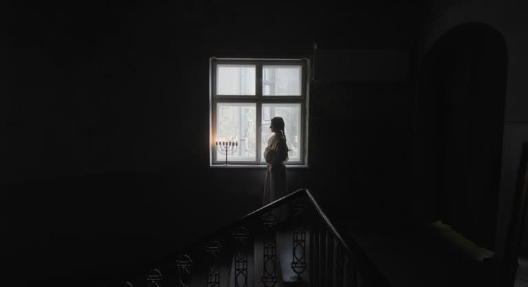 Silhouette of Woman with Candles by Window in Dark Room