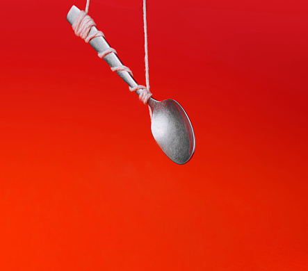 Silver spoon tied with string against a vibrant red backdrop, creating an illusion of floating
