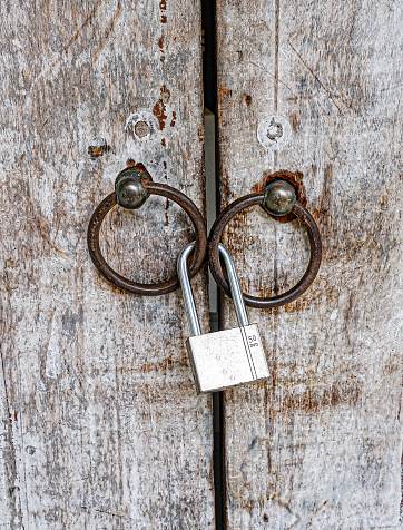 Old weathered wood doors with rusted round door knob loops and silver steel padlock