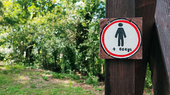 Restrictive sign with the image of a human symbol and a weight limit of 60 kg against the background of nature. Beauty standards and weight limits for people