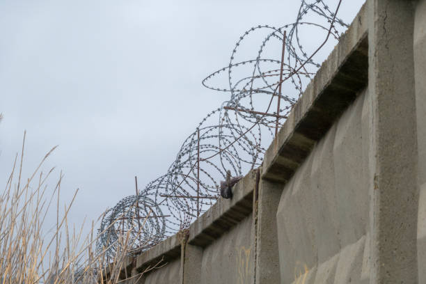istock Barbed wire over a concrete wall against the background of a cloudy sky 2151126826