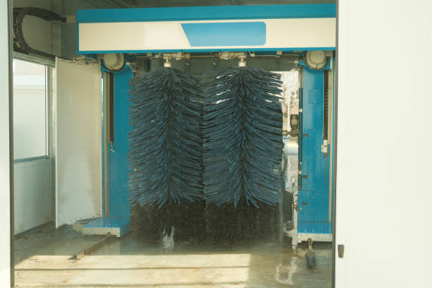 Front view of a black car being washed in an automatic car wash with green rotating brushes
