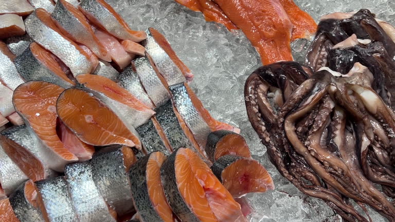 Top view of sliced ​​red salmon and octopus fish lying in ice on a store counter. Concept of fresh food in a store.