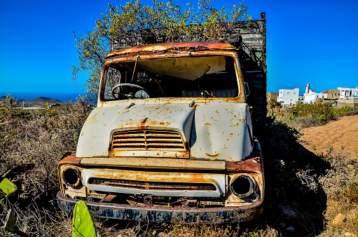 An old, rusted truck is sitting in a field. The truck is covered in weeds and has a lot of rust on it. The scene is desolate and abandoned, with no one around to see the truck