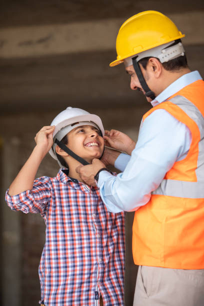 Mid adult male architect wearing hardhat to excited elementary son while standing in construction building