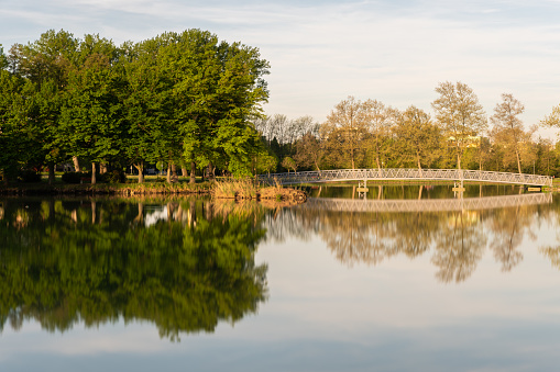 Long exposure shot of a small island with a bridge in the Boating Lake in Ajka in the morning in springtime.