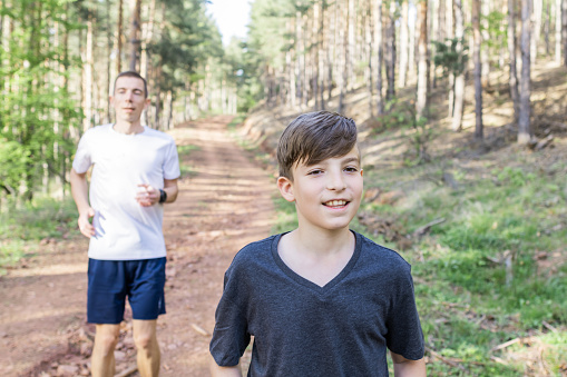 Happy father and son are running and exercising in forest. They are stretching and enjoying together outside. Sport lifestyle.