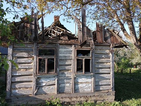 An old wooden ruined road house next to which a large walnut tree grows. The village house has been destroyed by time with a badly damaged roof and broken windows.