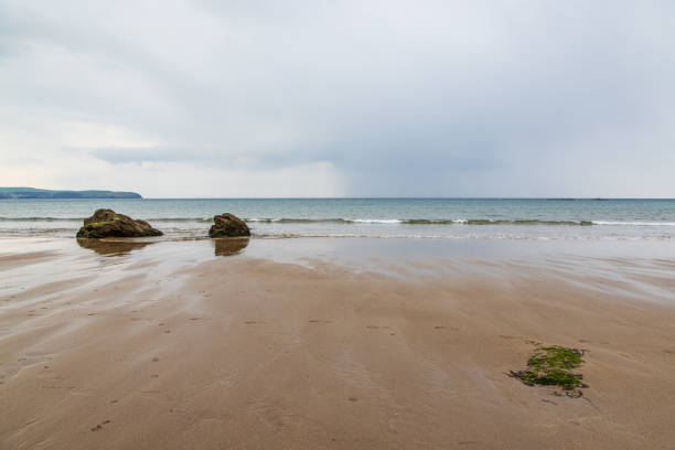 Incoming tide washes up Llanddwyn beach in Anglesey on a dark, cloudy spring afternoon.
