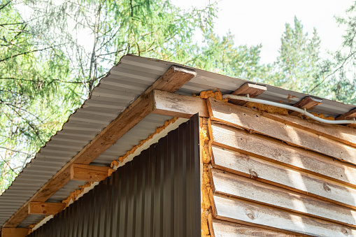 Hut constructed with unfinished wooden planks and corrugated metal sheets with foam insulation, located in a forested area