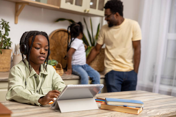 istock Little girl sitting at table working on her homework assignment using her tablet at home 2151152978