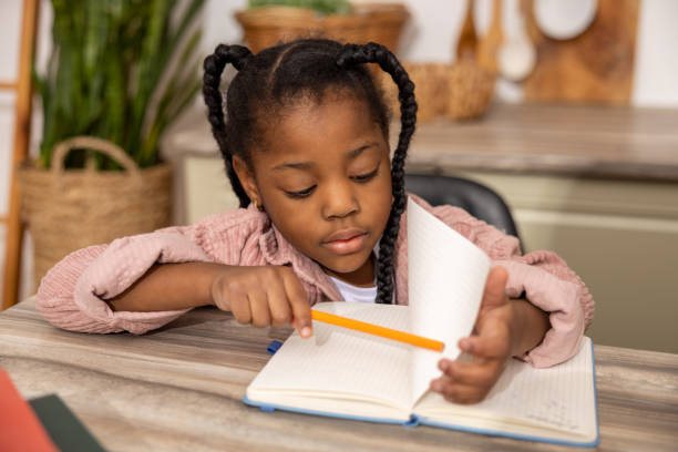 Serious multicultural girl with pen and book doing homework at home